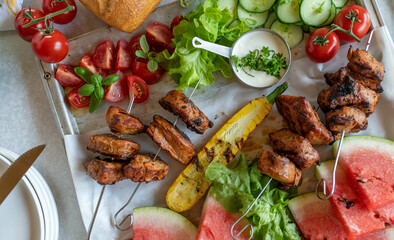 Grilled shish kebab on skewers with fresh vegetables, watermelon and yogurt sauce