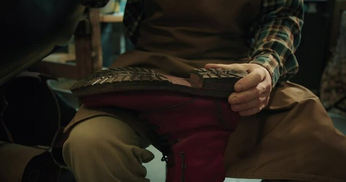 Young bootmaker drive in nails in a red shoe at the private workshop. 
