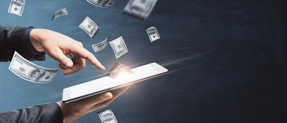 Winning online lottery or on bets on sports concept with man hand holding digital tablet with money rain on dark background