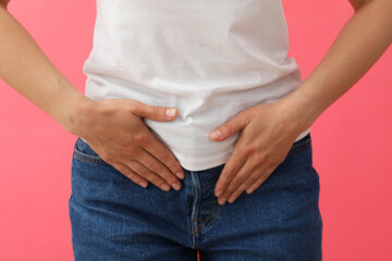 Woman pain, lower abdomen, holding hand on pink background