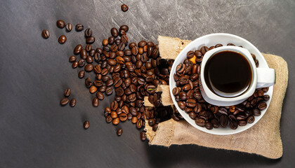 cup of coffee and coffee beans in a sack on dark background, top view