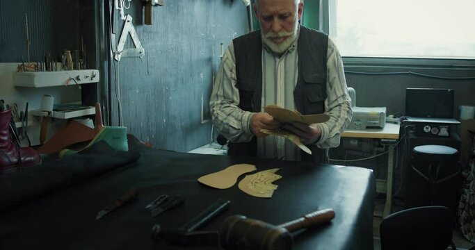 Mature shoemaker preparing patterns and tools for work at the workshop.