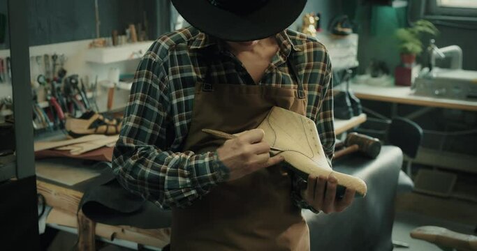 Male shoemaker cutting out pattern on a shoe last at the workshop.