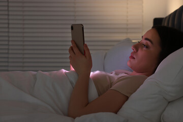 Young woman using modern smartphone in bed at night. Internet addiction
