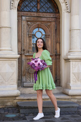 Beautiful woman with bouquet of spring flowers near building outdoors