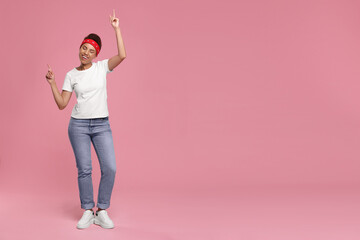 Happy young woman in stylish headband dancing on pink background. Space for text