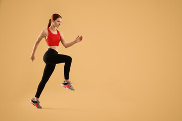 Fototapeta na wymiar Young woman in sportswear running on beige background, space for text