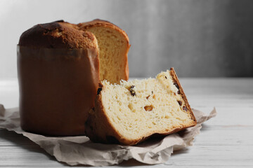 Delicious cut Panettone cake with raisins on white wooden table, space for text. Traditional Italian pastry