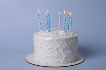 Delicious cake with cream and burning candles on light blue background