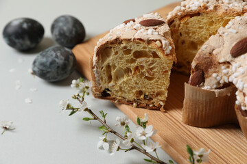 Pieces of delicious Italian Easter dove cake (traditional Colomba di Pasqua), branch with flowers and painted eggs on light grey table, closeup