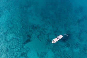 Aerial view of a yacht boat with vacationers and majestic blue sea with patterns on the bottom