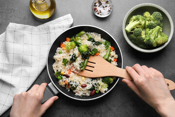 Woman taking tasty fried rice with vegetables at black table, top view