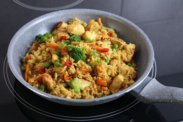 Tasty rice with meat and vegetables in frying pan on induction stove, closeup