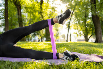 Girl legs with rubber elastic band during workout outdoors. Young womane exercising with additional equipment