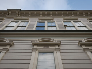 The facade of an apartment building in the Bay Area, showing classic San Francisco architecture such as Beaux Arts details. Blue skies with soft white clouds are reflected in the windows.