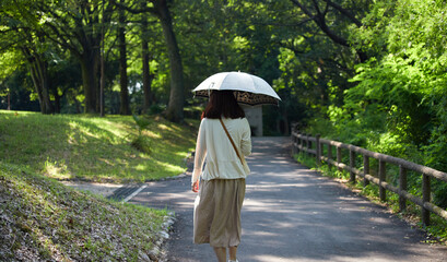 真夏の公園で日傘を持って散歩している若い女性の後姿