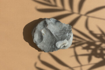 An empty podium made of gray stone on a beige background with a shadow of tropical leaves. Scene for the promotion of products, beauty, natural eco-cosmetics. Showcase, display case.