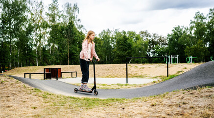 Preteen girl riding scooter on ramp in the park. Cute child with eco vehicle outdoors