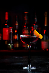 Adonis alcoholic cocktail drink with sherry and red vermouth, black bar counter background, steel tools and bottles