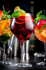 Red, white, rose sangria summer alcoholic cocktail drinks with spanish wine, fruits, citrus and ice. Black bar counter background, steel bar tools and bottles