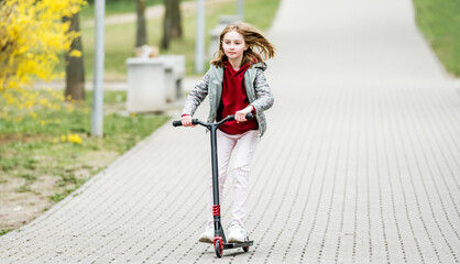 Little cute girl riding a scooter on a path in the park
