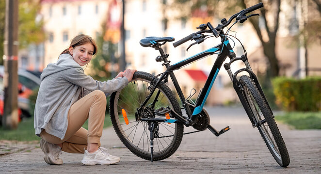 Young Girl Checking Pressure Of Bike's Tyres In The Autumn Park, Smilling And Looking Into The Camera.