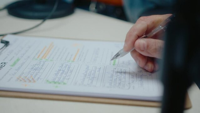 Hands of man sitting at a desk in the recording studio, planning podcast episodes, writing down tasks and ideas on paper sheet. Close-up shot