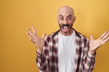 Naklejka premium Hispanic man with beard standing over yellow background celebrating crazy and amazed for success with arms raised and open eyes screaming excited. winner concept
