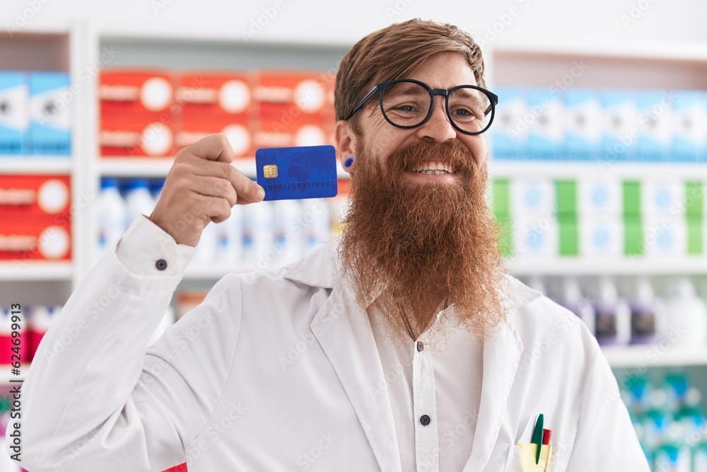 Sticker Young redhead man pharmacist smiling confident holding credit card at pharmacy