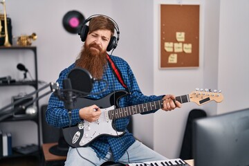 Young redhead man musician singing song playing electrical guitar at music studio