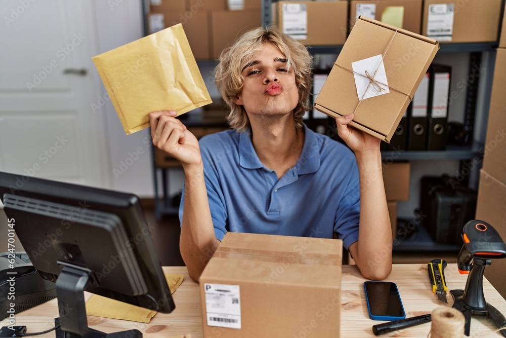 Sticker young man working at small business ecommerce holding packages looking at the camera blowing a kiss 