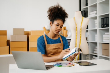 Startup small business SME, Entrepreneur owner African woman using smartphone or tablet taking receive and checking online purchase shopping order to preparing pack product box. in office.