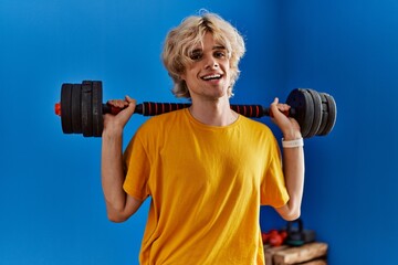 Fototapeta na wymiar Young blond man smiling confident using weight training at sport center