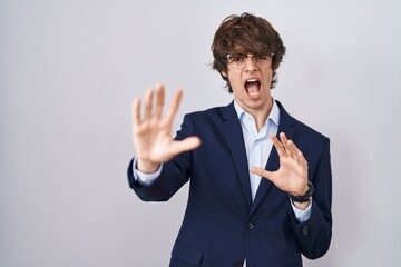 Hispanic business young man wearing glasses afraid and terrified with fear expression stop gesture with hands, shouting in shock. panic concept.