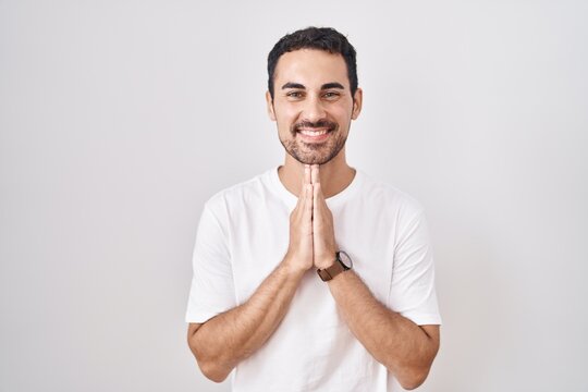 Handsome hispanic man standing over white background praying with hands together asking for forgiveness smiling confident.