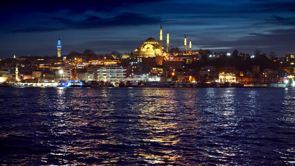 Istanbul, Turkey - February 2023: calm sea waves in Bosphorus reflecting Ayasofya Mosque and illuminated seaside restaurants