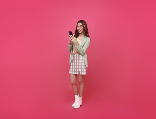 Happy smile Asian teen woman using smartphone device browsing media multimedia isolated on pink background.