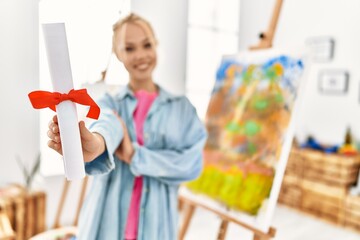 Young caucasian woman artist smiling confident holding diploma at art studio