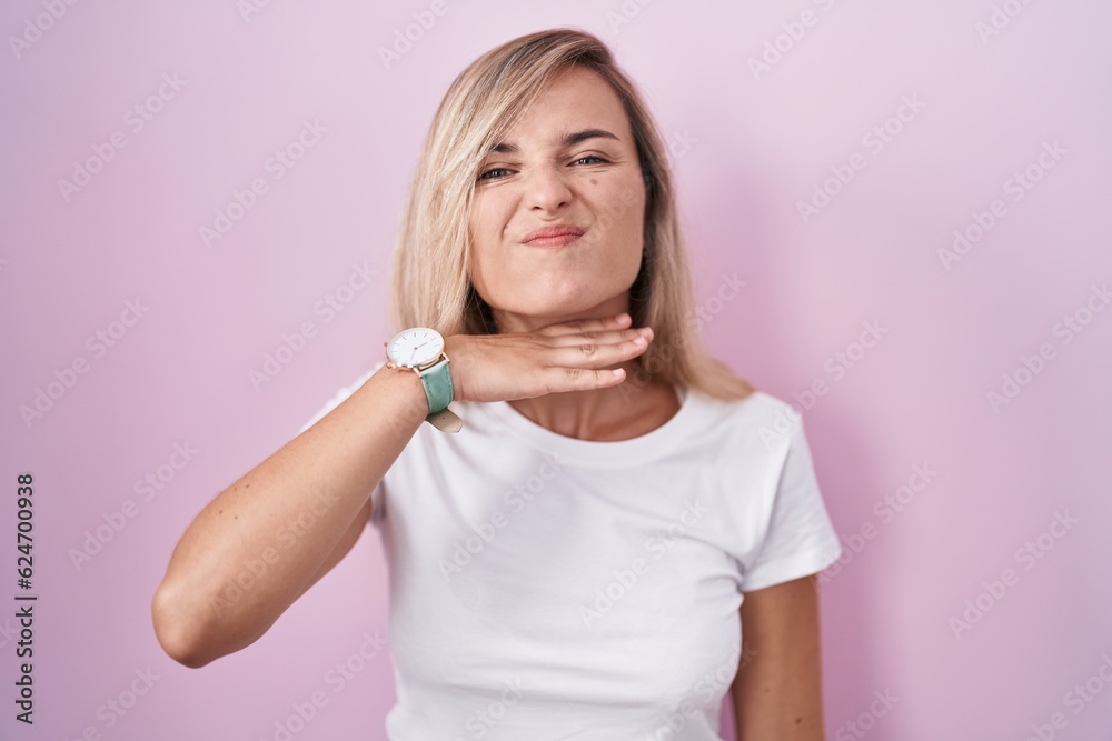 Sticker Young blonde woman standing over pink background cutting throat with hand as knife, threaten aggression with furious violence