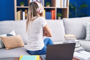 Obraz premium Young blonde woman studying using computer laptop at home standing backwards looking away with crossed arms