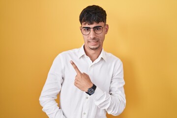 Young hispanic man standing over yellow background pointing aside worried and nervous with forefinger, concerned and surprised expression