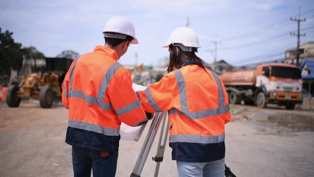 Surveyor engineers wearing safety uniform ,helmet and radio communication with equipment theodolite to measurement positioning on the construction site of the road with construct machinery background.
