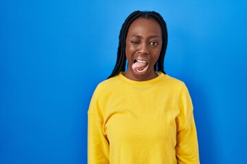 Beautiful black woman standing over blue background sticking tongue out happy with funny expression. emotion concept.