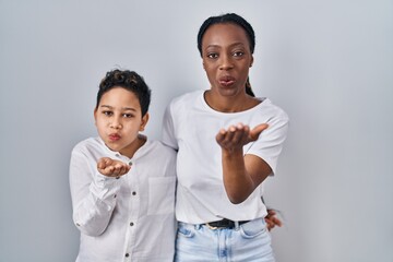 Young mother and son standing together over white background looking at the camera blowing a kiss with hand on air being lovely and sexy. love expression.