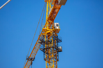 Naklejka premium Load-lifting crane on a construction site against the blue sky. A group of lifting platforms for construction and handling operations. Close-up of a basket for transporting people