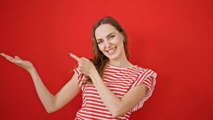 Young blonde woman smiling pointing to the side presenting over isolated red background