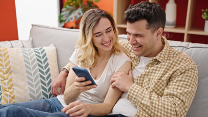 Man and woman couple using smartphone sitting on sofa at home