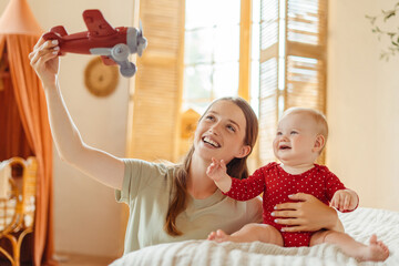 Young happy babysitter playing airplane with cute little baby child