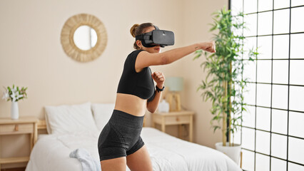 Young beautiful hispanic woman using virtual reality glasses boxing at bedroom