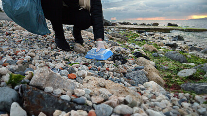 A female volunteer in action, walking on the beach and collecting litter in a bag to keep the coast...